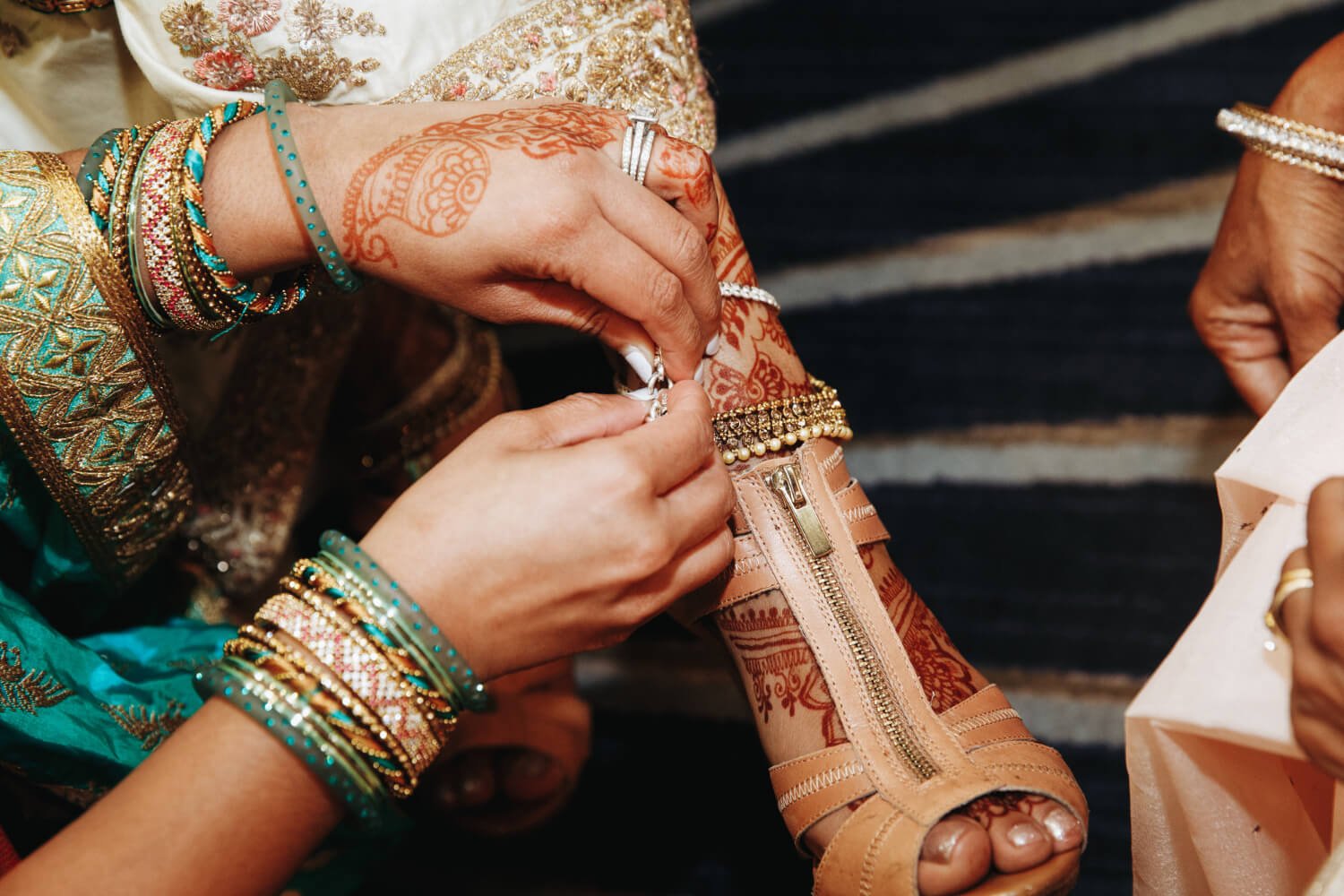 Une femme lace les chaussures de la mariée pendant qu'elle s'imprègne d'un parfum pour un mariage marocain. Ce parfum est en vente sur le site Majestia, spécialiste de la location de caftan marocain.